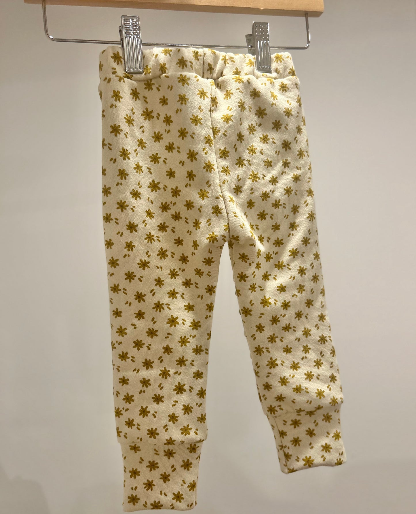 Handmade yellow jogger pants with pockets. These pants feature a gold floral pattern hanging on a rack against a plain background from Bella Rain Boutique. A handmade kids clothing boutique for kids in sizes NB-10. ,