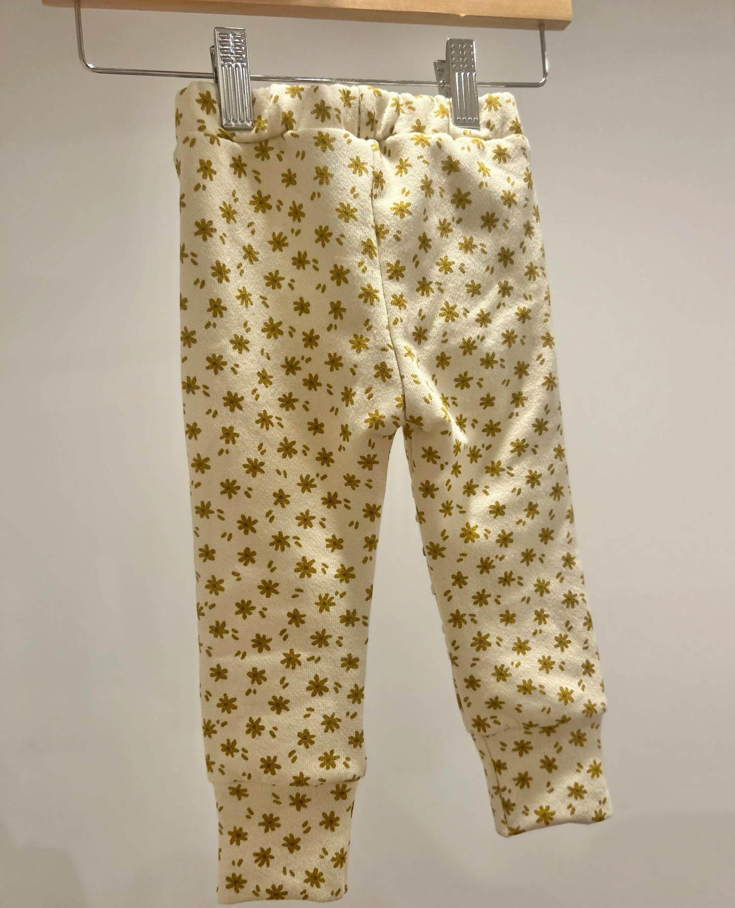 Handmade yellow jogger pants with pockets. These pants feature a gold floral pattern hanging on a rack against a plain background from Bella Rain Boutique. A handmade kids clothing boutique for kids in sizes NB-10. ,