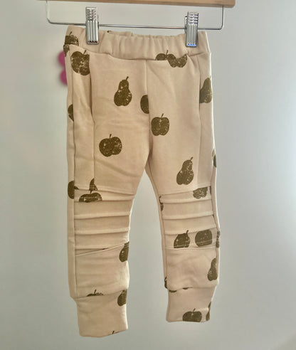 Beige baby pocket jogger pants with green pear patterns on a hanger against a plain background