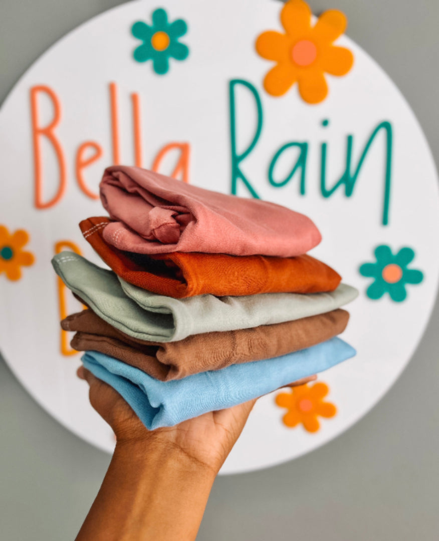 Stack of folded clothes held in front of a decorative plate with 'Bella Rain' text